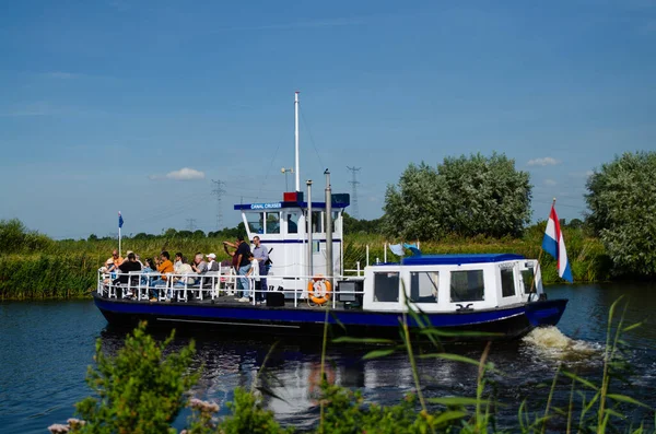 Kinderdijk, Hollanda, Ağustos 2019. Bir gezi teknesi, bölgenin tarihi yel değirmenlerini ziyaret etmek için Hollanda kırsal kesimindeki kanalları geziyor. Güneşli güzel bir gün, tekne kalabalık..