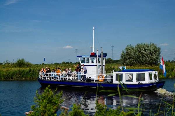 Kinderdijk, Hollanda, Ağustos 2019. Bir gezi teknesi, bölgenin tarihi yel değirmenlerini ziyaret etmek için Hollanda kırsal kesimindeki kanalları geziyor. Güneşli güzel bir gün, tekne kalabalık..