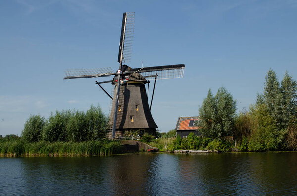 Kinderdijk, The Netherlands, August 2019. On a beautiful summer day a historic windmill, in perfect condition, in the Dutch countryside furrowed by canals lined with tall green grasses.