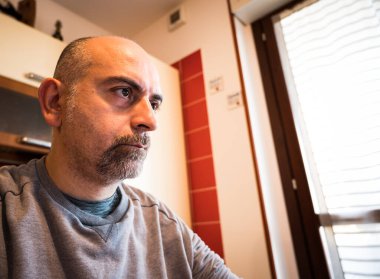 Evden çalışma: Kafkas bir adamın işine odaklanmış portresi. Bakışlar ekrana doğru hareket ediyor, değişen ekran ışığının yansıması yüzünden anlaşılıyor. Bulanık arka planda mutfak var.
