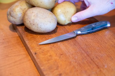 Evdeki hayat sahneleri: mutfakta patates salatası hazırlamak. Kesme tahtasının üzerinde patatesler çoktan kaynamış ve soğumuş, eller birini kavrıyor ve önce bir bıçakla kabuğunu kesiyor ve sonra kabuğunu soyuyor..