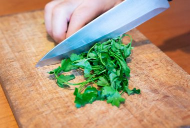 Evdeki hayat sahneleri: mutfakta doğranmış maydanozu kesme tahtasına hazırlamak. Bir el maydanozu tutarken, büyük bıçak onu güzelce mayınlıyor..