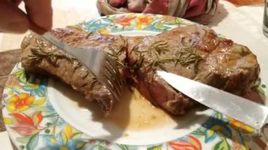 Büyük bir biftek pişirildi ve biberiyeyle tatlandırıldı. Hala tabakta sigara içiyor, bıçak ve çatal tutarlılığı kontrol ediyor. Arka planda masa hazır. 25fps