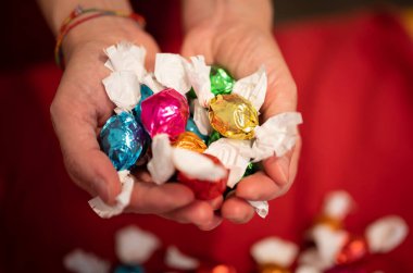 Parlak ve canlı renklere bürünmüş çikolatalı pralin dolu ellerin kavramsal görüntüsü. Noel ve tatiller.