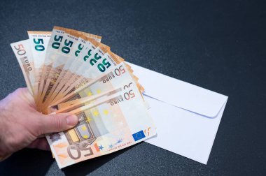 Siyah bir masada beyaz bir maaş çeki açıldı: 50 avroluk banknotları tutan eller vantilatör şeklinde düzenliyor. Maaş kavramsal resim.