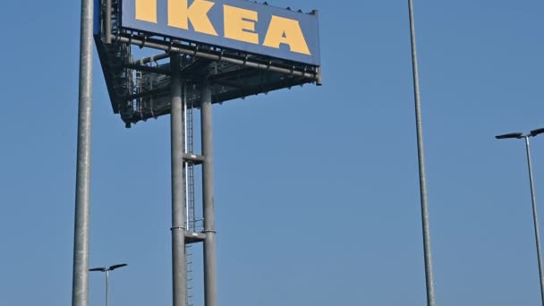 Collegno, Torino bölgesi, İtalya. Ocak 2021. Güneşli bir günde, büyük IKEA logosunun görüntüsü alışveriş merkezinin önündeki çok uzun bir direğin üstünden geçiyor.. — Stok video