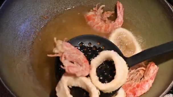 家庭生活场景 用热油油炸虾仁和烤鱿鱼圈的特写镜头 用一只黑色的撇子把它们从锅里捞出来 — 图库视频影像