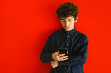 Sarı stüdyo arka planında cep telefonu olan sevimli kahverengi kıvırcık saçlı çocuk, mobil uygulamalar kullanıyor ya da arkadaşlarıyla sohbet ediyor, kopyalama alanı. Akıllı telefon kullanma kavramı, cihazlara bağımlılık.