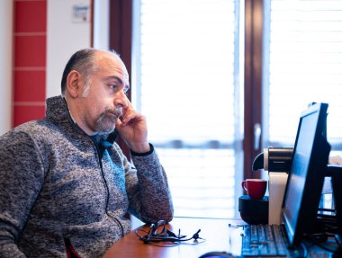 A middle aged caucasian man working from home, is pissed off and feels isolated. Concept of stressful and demeaning work. Consequences of social distancing for the coronavirus.