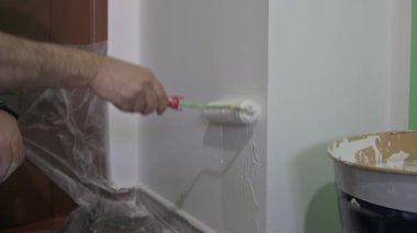 Beyazlık kazandırmak için tekerleğin sapına yakın çekim. Erkek el, duvara geçirmek için onu yakalar: silindiri dağıtırken damlayan bazı boya damlalarını görebilirsiniz. Ev yenileme konsepti.