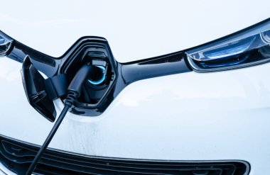 Strasbourg, Fransa. Ağustos 2019. Bir Renault Zoe park etmiş ve şarj istasyonuna bağlı. Fiş arabanın burnunun ortasına sığıyor, araba üreticisinin logosu kapak görevi görüyor..