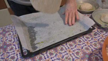 Ev yapımı pizza. Taze pizza hamuru onu tavaya yaymak için kullanılır: beyaz bir adamın elleri taze hamur topunu ezer. Yanında, hamurlu iki tava daha var..