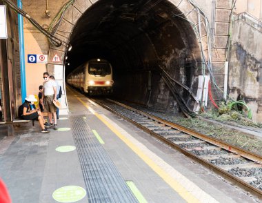 Vernazza, Liguria, İtalya. Haziran 2021. Tren istasyonu tünel çıkışının bitişiğindedir. Tren geliyor, gezginler platformda bekliyor. Koronavirüs maskeleri var..