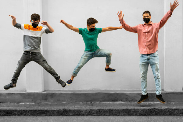 Young people jumping outdoor during coronavirus outbreak. Happy friends wearing face protective masks and having fun together. Social distancing,happiness concept, new normal. Millennials lifestyle.