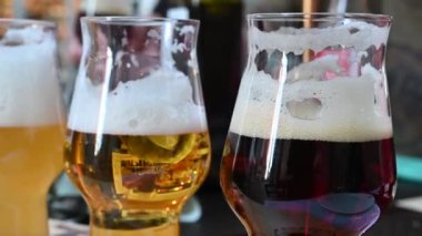 Bira fabrikasında farklı renkte bardaklar ve içkinin opaklığıyla tatmak. Arkaplan, bulanık ve ayırt edilemez, tava hareketi. Bir yaşam tarzı olarak tatma kavramı.
