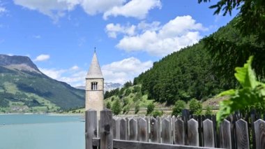 Curon, İtalya, Haziran 2021. Curon 'un (Graun) eski çan kulesinin güzel yaz günündeki görüntüleri Resia Gölü' nün sularından yükseliyor. İki turist, bir kadın ve bir oğlan, fotoğrafını çek..