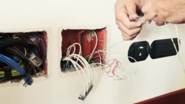 İşteki bir elektrikçi: iki kabloyu boruların içine sokmak için elleriyle bağlıyor..