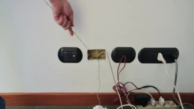 İşteki bir elektrikçi: elleriyle bağlantı kutusundan bir kablo çekiyor, boruların içine diğer uca bağlanmış olan yeni kabloyu sürüklüyor..