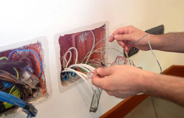 An electrician at work: with his hands he connects two cables to be able to slide them inside the pipes.