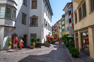 Bolzano, İtalya, Haziran 2021. Tarihi merkezde ikinci bir cadde. Sokaktaki insanlar, arka planda parlak, sıcak renkli yüzler. Güzel bir yaz günü.