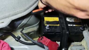 Bagajında konut olan araba aküsü değişimi. Elektrikçi, akü konut desteğinin vidalarını bir anahtarla söker..