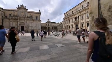 Lecce, Puglia, İtalya. Ağustos 2021. Katedral meydanında yürürken çekilen görüntüler. İnsanlarla, kiralık bisikletlerle ve akıllı telefonuyla fotoğraf çeken bir adamla tanışıyoruz. Güzel bir yaz günü.