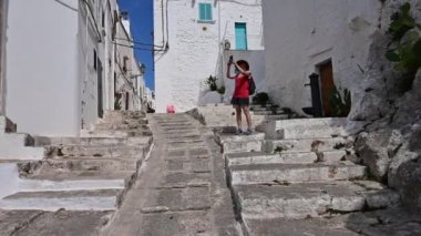 Ostuni, Puglia, İtalya 'nın beyaz sokaklarında inanılmaz pov görüntüleri. Karakteristik merdivenleri çıkarken akıllı telefonuyla fotoğraf çekmek isteyen orta yaşlı bir kadınla karşılaştık..