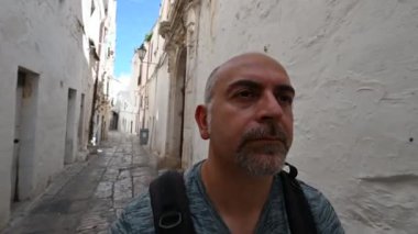 İtalya 'nın Puglia, Ostuni kentinin beyaz sokaklarında pov görüntüleri. Orta yaşlı bir turist, tarihi merkezin karakteristik bir sokağında yürüyor. Seyahat ve keşif konsepti.