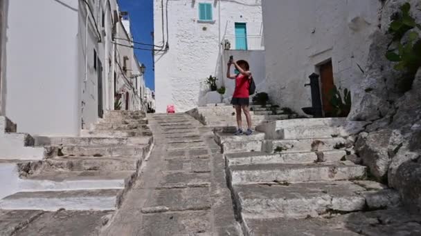 オストゥーニ プーリア州 イタリアの白い路地で驚くべきPov映像 特徴的な階段を登る私たちは中年の女性が彼女のスマートフォンで写真を撮ることを意図して満たしています — ストック動画