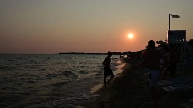 Kavramsal görüntü: alacakaranlıkta bazı çocuklar suyun kenarında top oynarlar. Rahatlama ve arkadaşlık tatili konsepti. Yavaş çekim.