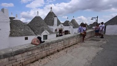 Alberobello, Puglia, İtalya. Ağustos 2021. Büyüleyici tarihi köydeki Pov görüntüleri. Konik taştan çatısı olan küçük beyaz trulli 'ye doğru yürüyen bir ara sokağı araştırıyoruz. Turistler selfie çeker..