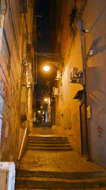 Napoli, İtalya, 27 Aralık 2024. Tarihi merkezdeki bir ara sokağın dikey gece görüntüleri: sıcak sarı ışıklandırması ve retro atmosferi olan eşsiz bir cazibe. Şehri keşfetmek ve keşfetmek..