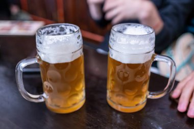 Prag, Çek Cumhuriyeti, 7 Ağustos 2023. Yan yana iki bardak bira. Bulanık arka planda, zevk alanların elleri. Paylaşılan içkinin yaşam tarzı.