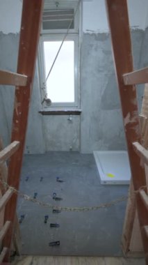 Banyo tadilatı devam ediyor: merdivenlerin altındaki POV manzarası mavi ve siyah yer kaplamalı gri fayansları ve beyaz duş tepsisini ön plana çıkarıyor. Sıva kaplı duvarlar. Yenileme konsepti.