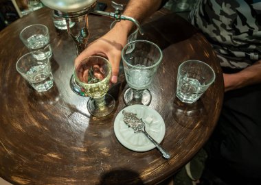 Prag, Çek Cumhuriyeti, 8 Ağustos 2023. İçinde absent olan bir masa ve bir bardak su. Bir el yeşil likörün bardağını tutuyor, yanında özel bir kaşık ve şeker küpü..