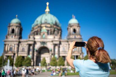 Berlin, Almanya, 11 Ağustos 2023. Berlin Katedrali 'ni güneşli yaz gününde mavi gökyüzü ve arkasında tarihi şehir manzarasıyla fotoğraflayan bir kadın gezgin.