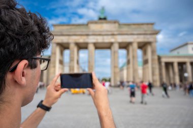Berlin, Almanya, 12 Ağustos 2023. Berlin 'in ünlü Brandenburg Kapısı' nı akıllı telefon, arka plan görüntüsü şehir turu ve seyahat anılarını kaydeden genç bir adam.