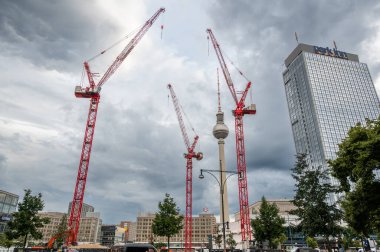 Berlin, Almanya, 12 Ağustos 2023. Berlin silueti, fernsehturm ve park otelinin etrafında birden fazla kırmızı vinç ile bulutlu gökyüzünün altında kentsel gelişimi gösteriyor.
