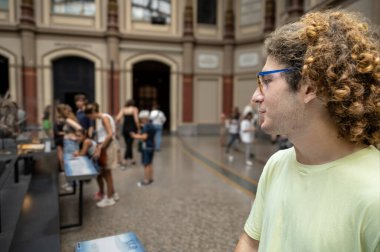 Berlin, Almanya, 15 Ağustos 2023. Kıvırcık saçlı ve gözlüklü bir adam Berlin 'deki doğal tarih müzesini keşfediyor, sergileri ve diğer ziyaretçileri inceliyor.