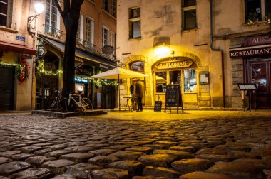 Lyon, Fransa. 28 Aralık 2023. Cobblestone Viux Lyon Caddesi 'nde canlı bir gece. Sıcak ışıklar tarihi binaları, barları ve büyüleyici akşam atmosferini aydınlatıyor.