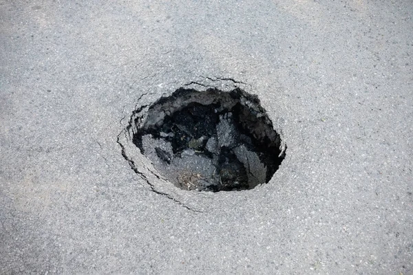 Round hole in gray asphalt, damaged road.