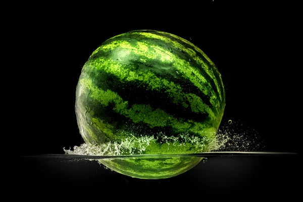 Frische Melone fällt in Wasser mit Spritzer auf schwarzem Hintergrund — Stockfoto