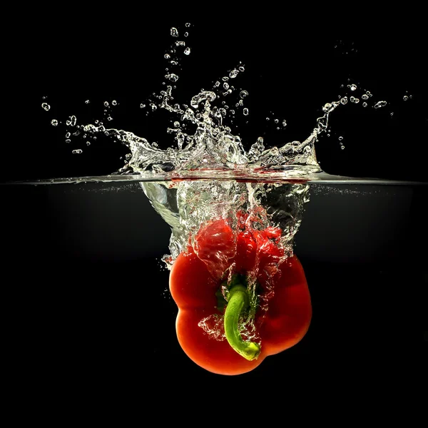 Rote Paprika fällt in Wasser mit Spritzer auf schwarzem Hintergrund — Stockfoto