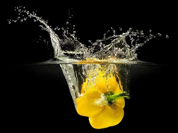 Gelbe Paprika fällt ins Wasser mit Spritzer auf schwarzem Hintergrund — Stockfoto