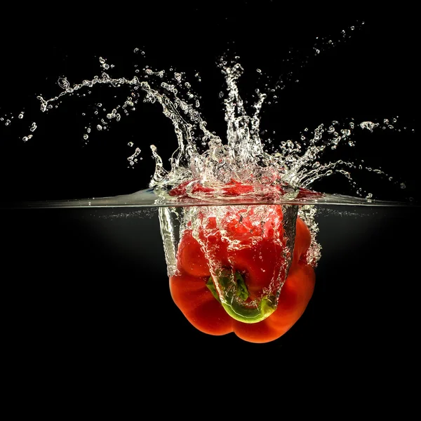 Rote Paprika fällt in Wasser mit Spritzer auf schwarzem Hintergrund — Stockfoto