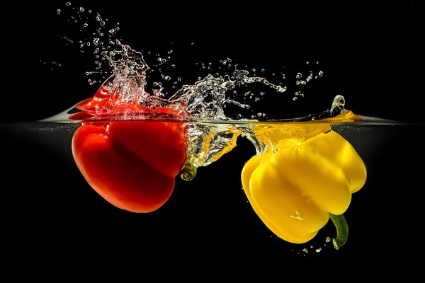 Gruppe von Paprika fällt in Wasser mit Spritzer auf schwarzem Hintergrund — Stockfoto