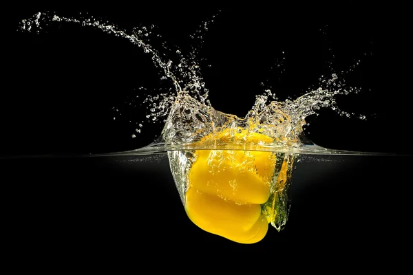 Жовтий болгарський перець падає у воду з бризкою на чорному тлі — стокове фото