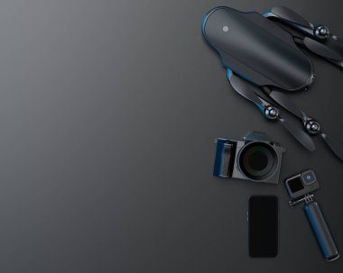 Tasarımcı çalışma alanının ve var olmayan DSLR kamera, cep telefonu, dron ve siyah arkaplanda selfie çubuğundaki aksiyon kamerası gibi teçhizatların üst görüntüsü. Canlı yayın için 3D aksesuar hazırlama