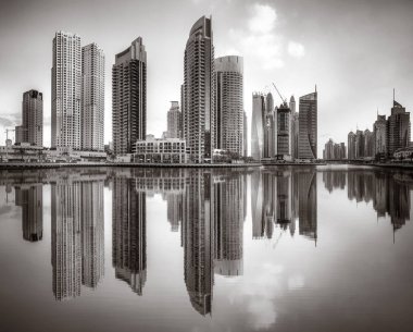 Tek renkli şehir gökdelenleri bulutlu bir gökyüzü altında sakin suyu yansıtan gökdelenler, kentsel gelişim konsepti, Dubai Marina Körfezi BAE