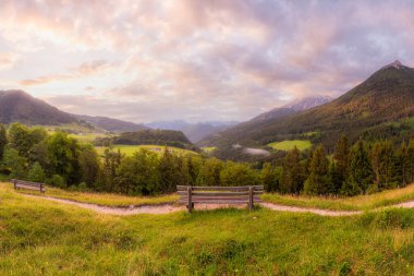 Berchtesgaden Ulusal Parkı, Yukarı Bavyera Alpleri, Almanya, Avrupa 'da gün batımında Hintersee Gölü yakınlarında yol ve bank ile Meadow. Gökyüzü yolu kırpılıyor